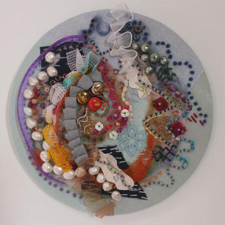 Circle abstract embroidery piece rock pool. Blue background with blue, pink, orange and purple embroidery.