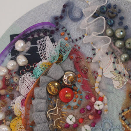 Circle abstract embroidery piece rock pool. Blue background with blue, pink, orange and purple embroidery.